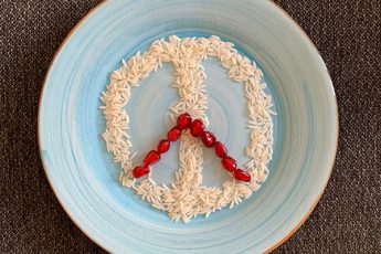 Peace sign made with rice grains and pomegranate arils on blue plate for Persian food blog