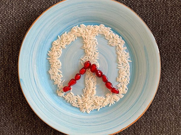 Peace sign made with rice grains and pomegranate arils on blue plate for Persian food blog